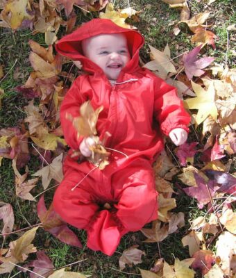 Young baby lying amongst Autumn leaves, keeping clean and dry in her Mud Mates NZ-made waterproof overalls and shoe covers. Save money with a Busy Crawler Pack