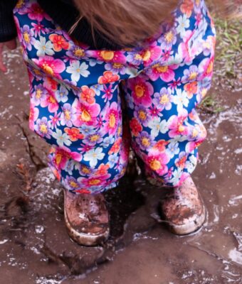 Child standing in a muddy puddle wearing floral overpants