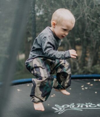 Young child bouncing on tramp wearing Mud Mates waterproof green camo children's overpants