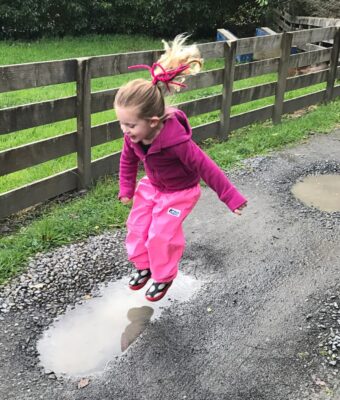 Young girl about to jump in a puddle, keeping clean and dry in her NZ-made waterproof overpants