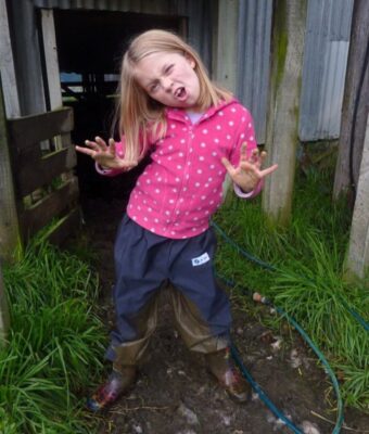 Child wearing navy waterproof overpants standing in mud outdoors