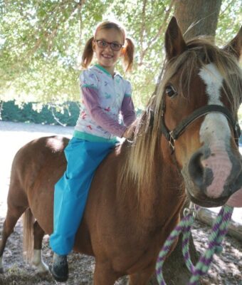 Young girl on a horse wearing Mud Mates NZ-made waterproof overpants