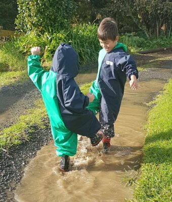 Children splashing in muddy puddles, keeping clean and dry in their Mud Mates waterproof childrens coveralls