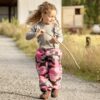 Young girl on a farm, walking, holding a stick wearing Mud Mates NZ- made waterproof overpants in pink camo