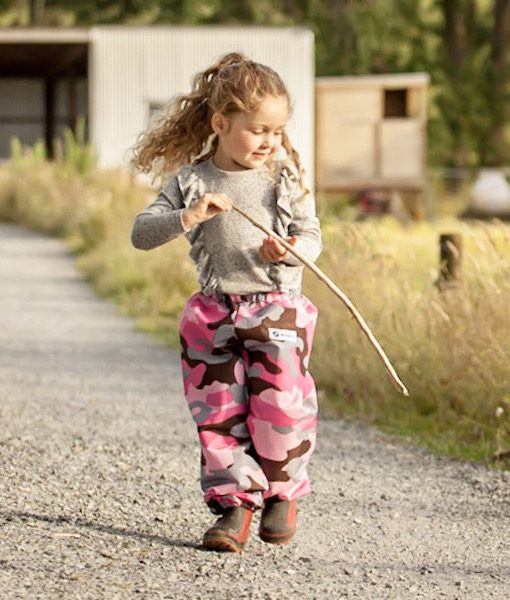 Young girl on a farm, walking, holding a stick wearing Mud Mates NZ- made waterproof overpants in pink camo