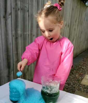 Young girl excited by a fizzing science experiment wearing a Mud Mates pink craft apron/art smock