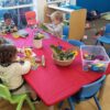 Red, rectangle NZ-made elasticated Fitted Tablecloth protecting a table at an early childcare centre.