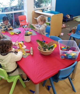Red, rectangle NZ-made elasticated Fitted Tablecloth protecting a table at an early childcare centre.