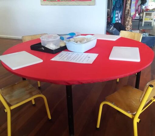 Red, round, NZ-made elasticated Fitted Tablecloth used for baking at an early childcare centre