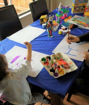 Kids painting at a dining room table protected with a Mud Mates elasticated fitted tablecloth