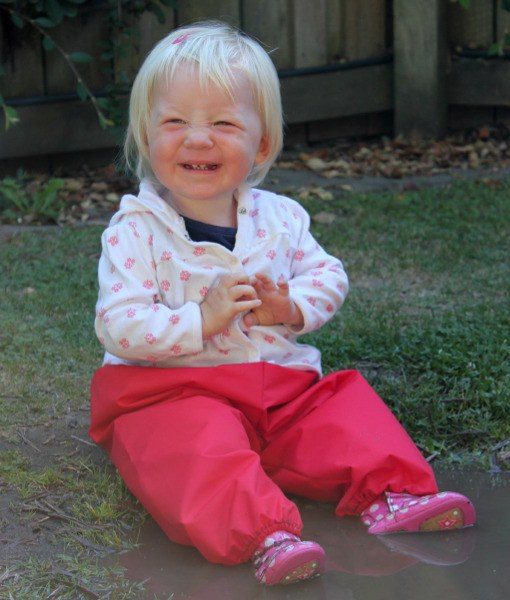 Young toddler sitting on grass wearing Mud Mates NZ-made waterproof overpants in red
