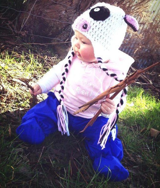 Baby sitting on grass wearing Mud Mates NZ-made waterproof overpants in royal blue