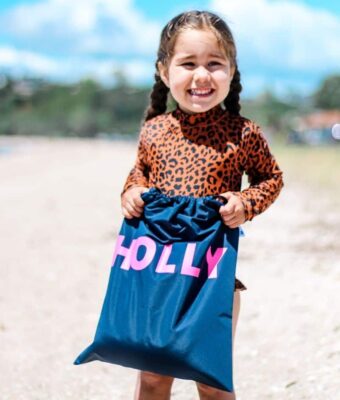 Young girl on beach holding her Mud Mates NZ-made waterproof swim bag