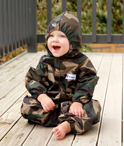 Young child sitting wearing Mud Mates NZ-made green camo waterproof coveralls