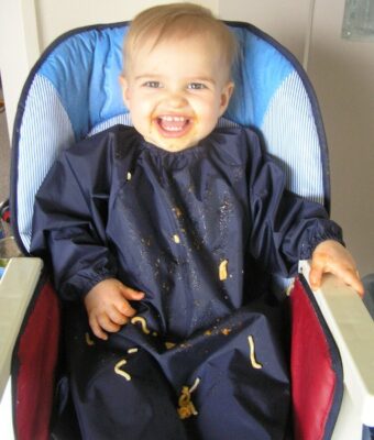 Baby in highchair messy with food wearing a Mud Mates NZ-made long sleeve bib