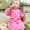Messy eating toddler wearing a pink Mud Mates long sleeve bib