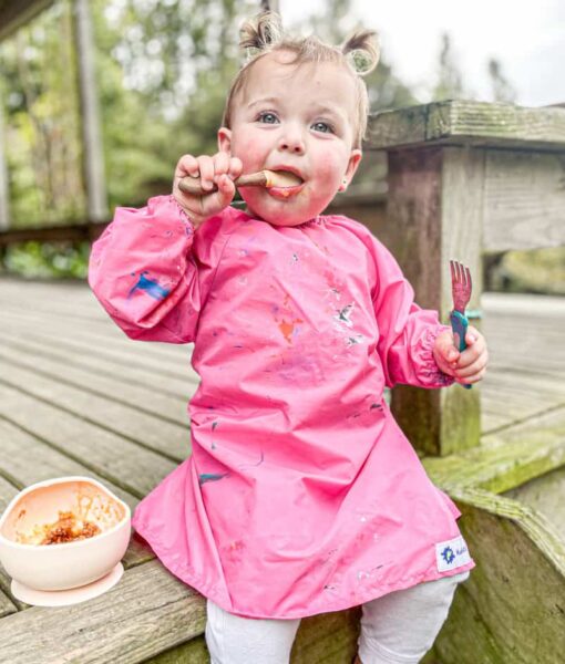 Messy eating toddler wearing a pink Mud Mates long sleeve bib