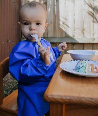 Toddler sitting at table wearing a NZ-made Long Sleeve Bib eating cake