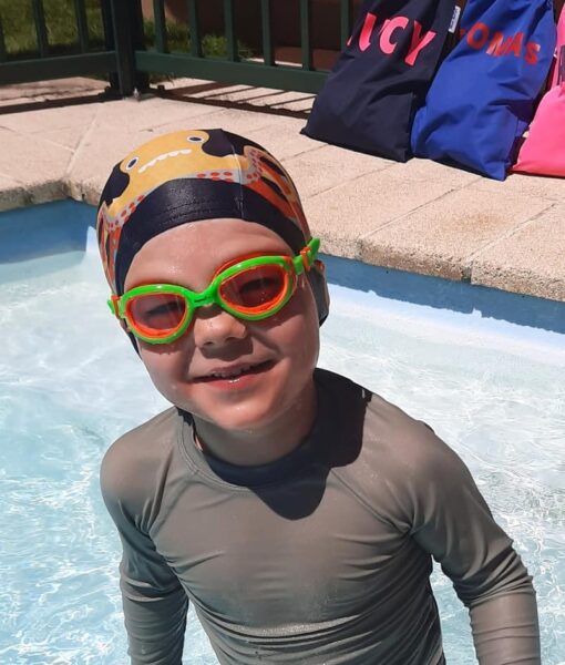 Young boy in swimming pool wearing Otto the Octopus lycra kids swim cap and Funkies orange/green kids goggles