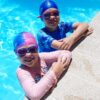 A girl and boy at edge of swimming pool wearing silicone kids swim caps and Funkies kids goggles