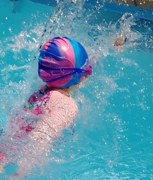 Girl swimming in pool wearing a pink/blue multi-coloured silicone swim cap