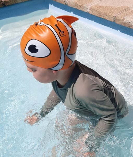 Young boy in swimming pool wearing an orange fish silicone kids swim cap