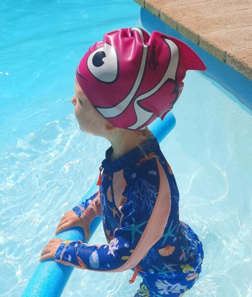 Toddler girl in swimming pool wearing a silicone pink fish swim cap