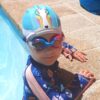 Toddler in swimming pool wearing rainbow drop unicorn lycra kids swim cap and goggles