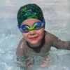 Toddler in swimming pool wearing a lycra swim cap and rainbow blue/green kids goggles