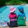 2 children sitting on the edge of a swimming pool with their personalised swim bags / wet bags
