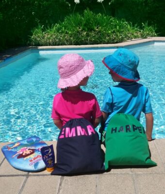 2 children sitting on the edge of a swimming pool with their personalised swim bags / wet bags
