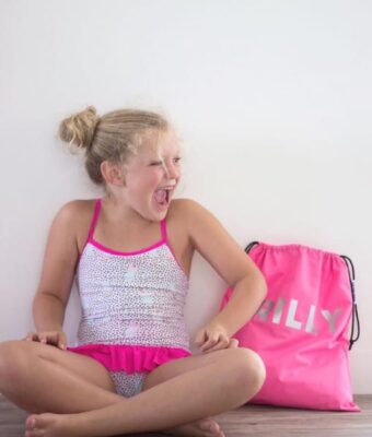 Girl in her togs sitting by her Mud Mates pink personalised swim bag / wet bag