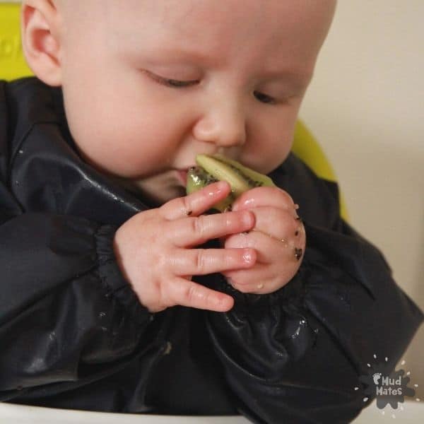 7 Tips for Baby Led Weaning Success: baby feeding himself a piece of kiwifruit