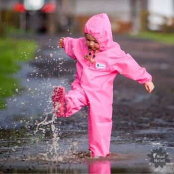Young girl wearing pink Mud Mates waterproof coveralls playing in puddles