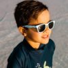 Fashionable young boy near water wearing Beachcomber Bicycle Ride kids sunglasses