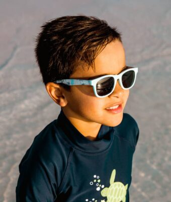 Fashionable young boy near water wearing Beachcomber Bicycle Ride kids sunglasses