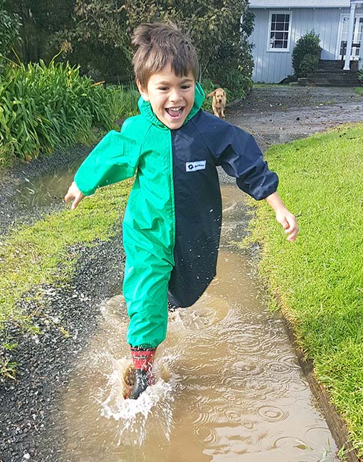 Why Choose Us? Young boy smiling, running through puddles wearing Mud Mates NZ-made kids waterproof overalls