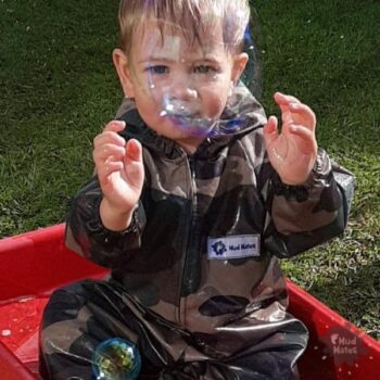 Toddler wearing Mud Mates NZ-made camo coveralls enjoying outdoor play and playing with bubbles