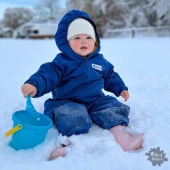 Toddler wearing Mud Mates waterproof coveralls playing with a bucket and spade on her first time on the snow
