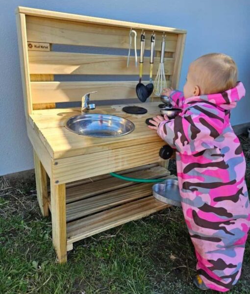 Young child wearing Mud Mates waterproof Coveralls playing at her NZ-made wooden Mud Kitchen