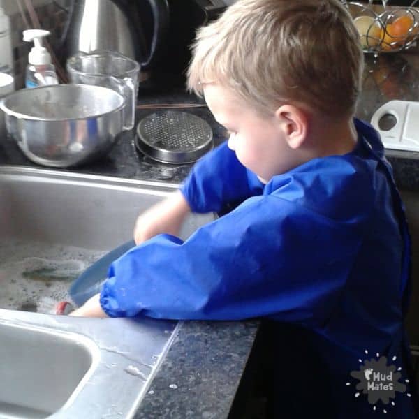 Young child standing at kitchen sink washing dishes: activities for toddlers in the kitchen