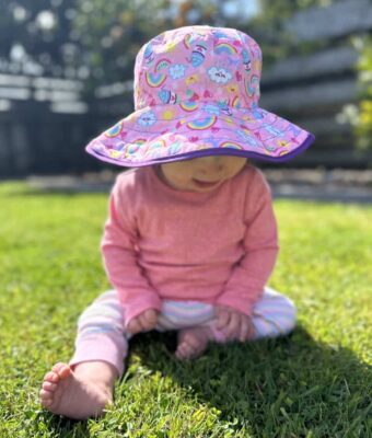 Baby wearing a Reversible kids sun hats - Rainbow pattern with solid purple on the reverse. UPF 50+ fabric for sun protection
