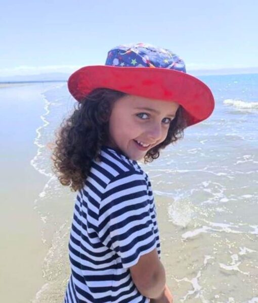 Young girl on the beach wearing a Space design reversible sun hat. Shop UPF 50+ reversible kids sun hats