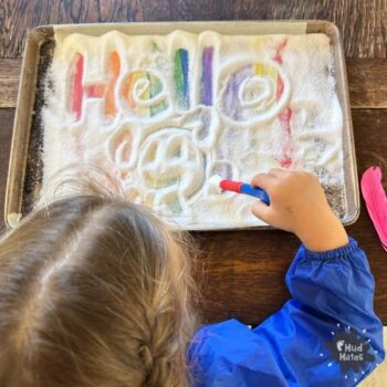 Young child using a paintbrush to write 'hello' in the salt using a rainbow salt writing tray