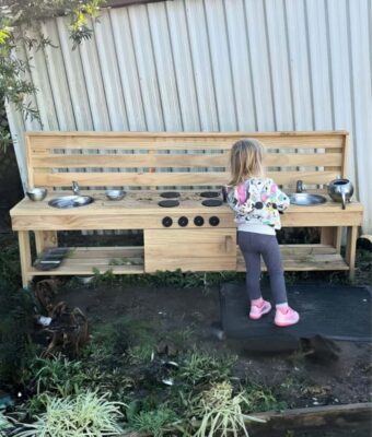 Young girl plays at her extra large wooden Mud Kitchen from Mud Mates