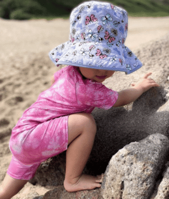 Toddler on the beach wearing Mud Mates Reversible kids sun hats - Butterfly pattern with solid lilac underside. UPF 50+ sun protection