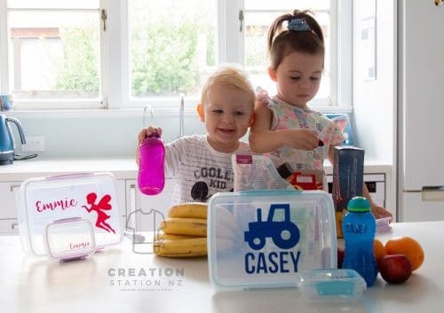 Clearly named lunchboxes and drink bottles on a kitchen bench