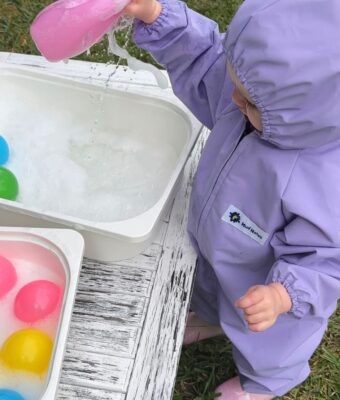 Young child enjoying water play - keeping dry in lilac her NZ-made waterproof children's coveralls