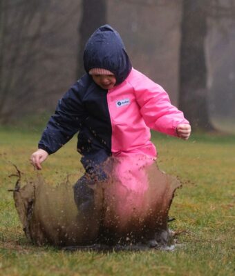 Child jumping in a big muddy puddle, wearing NZ-made navy/pink children's coveralls