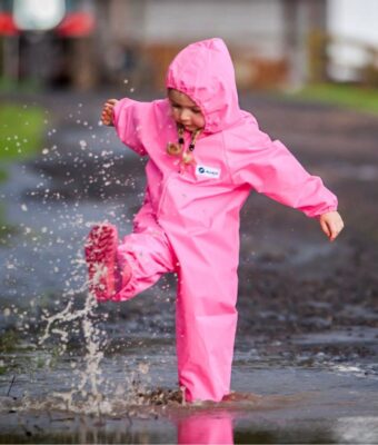 Girl splashing in a puddle, keeping dry wearing her pink Mud Mates NZ-made children's coveralls